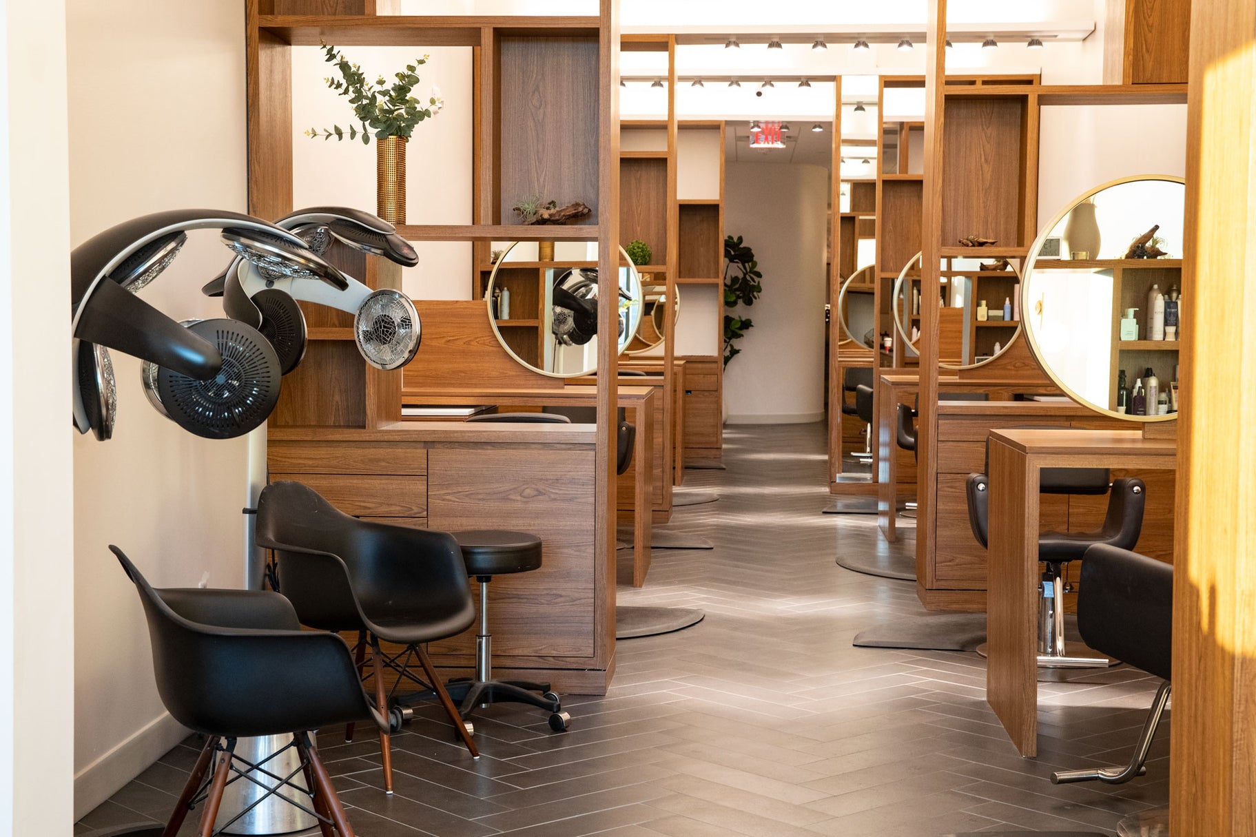 Salon interior with wooden stations, mirrors, and black chairs.