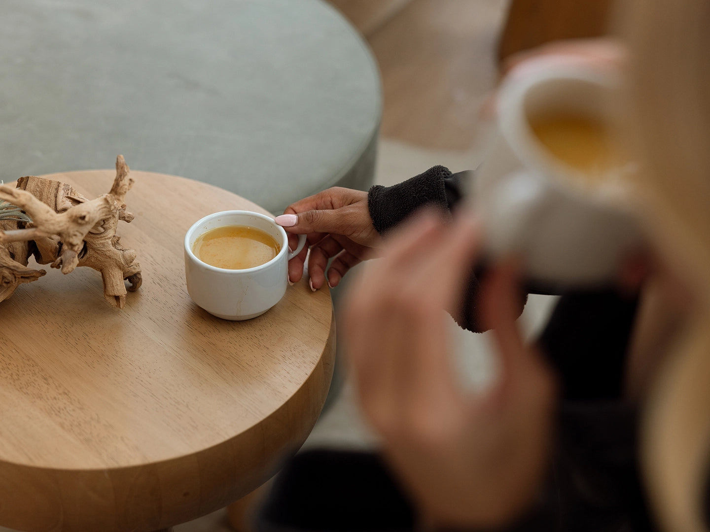Two people holding cups of coffee on a wooden table.