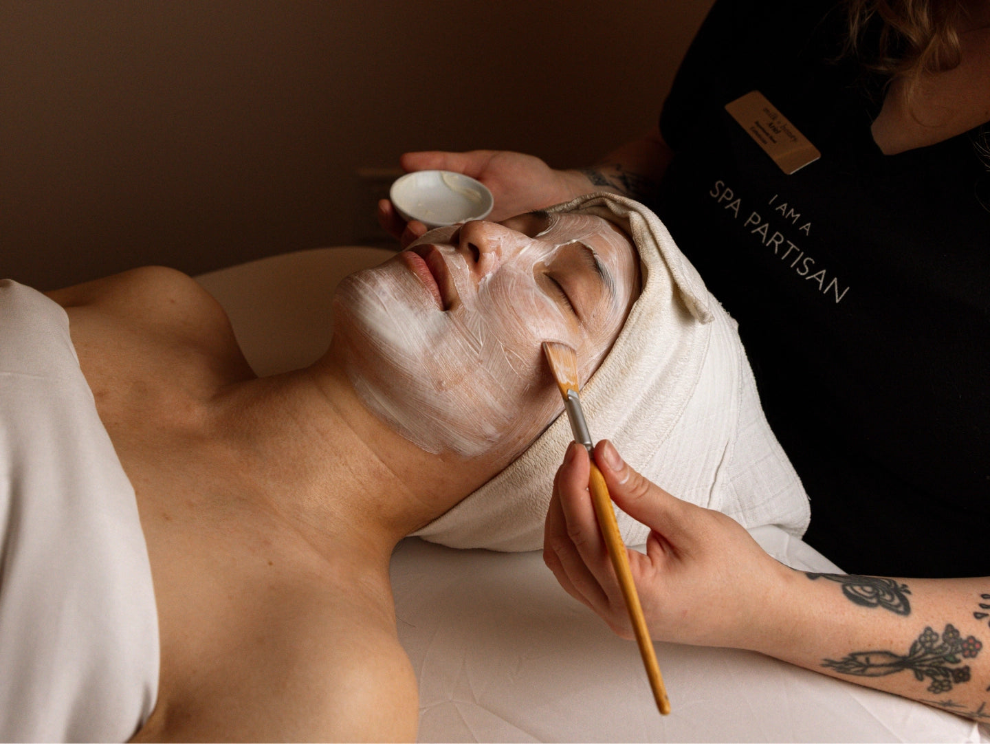 Person receiving a facial treatment with a professional applying cream to their face.