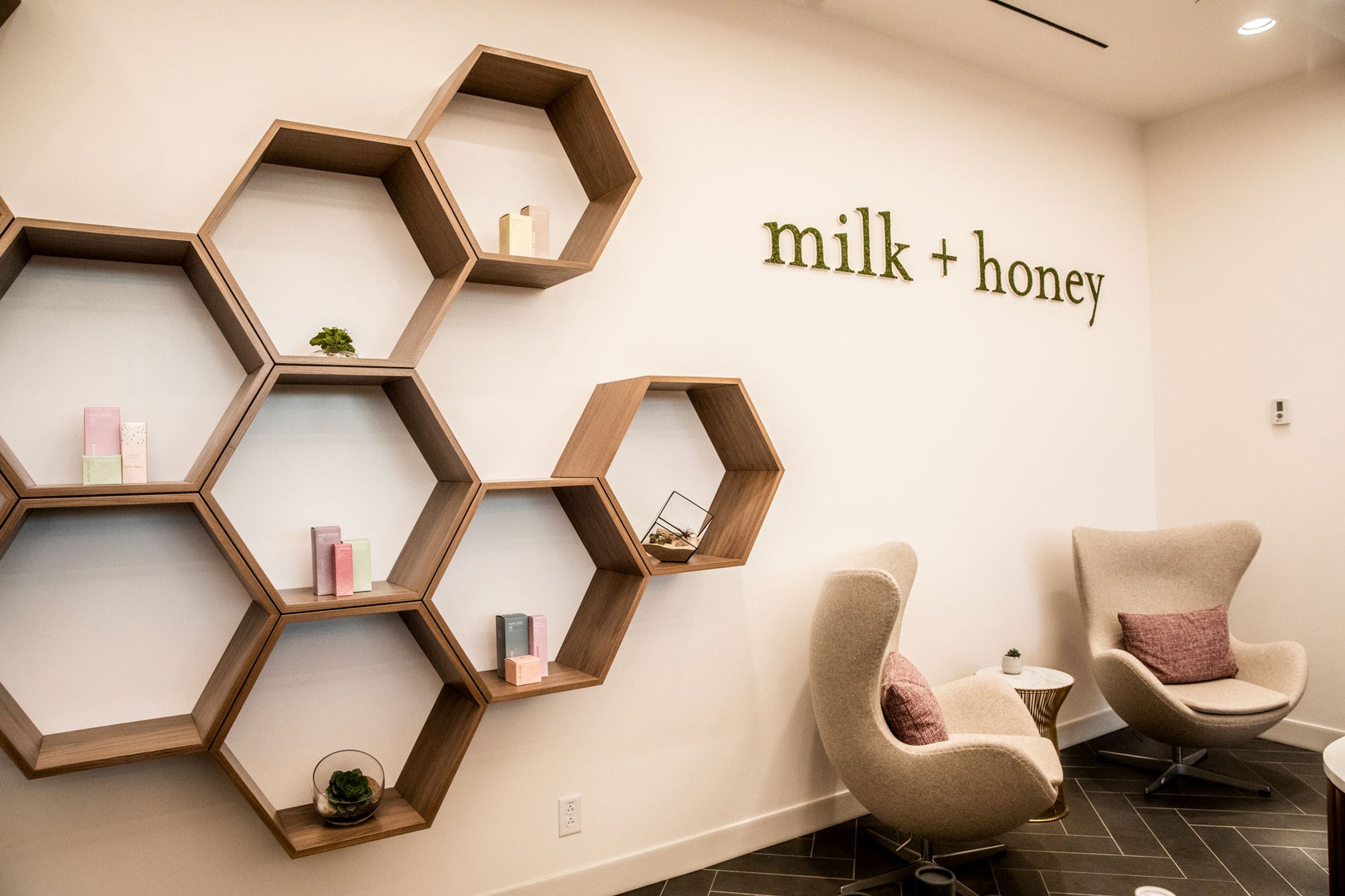 Modern interior with hexagonal shelves and 'milk + honey' sign on a wall.