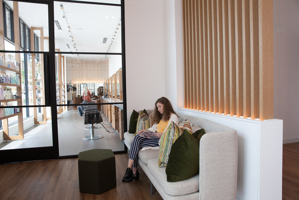 Woman reading a book on a couch in a modern interior setting with large windows.