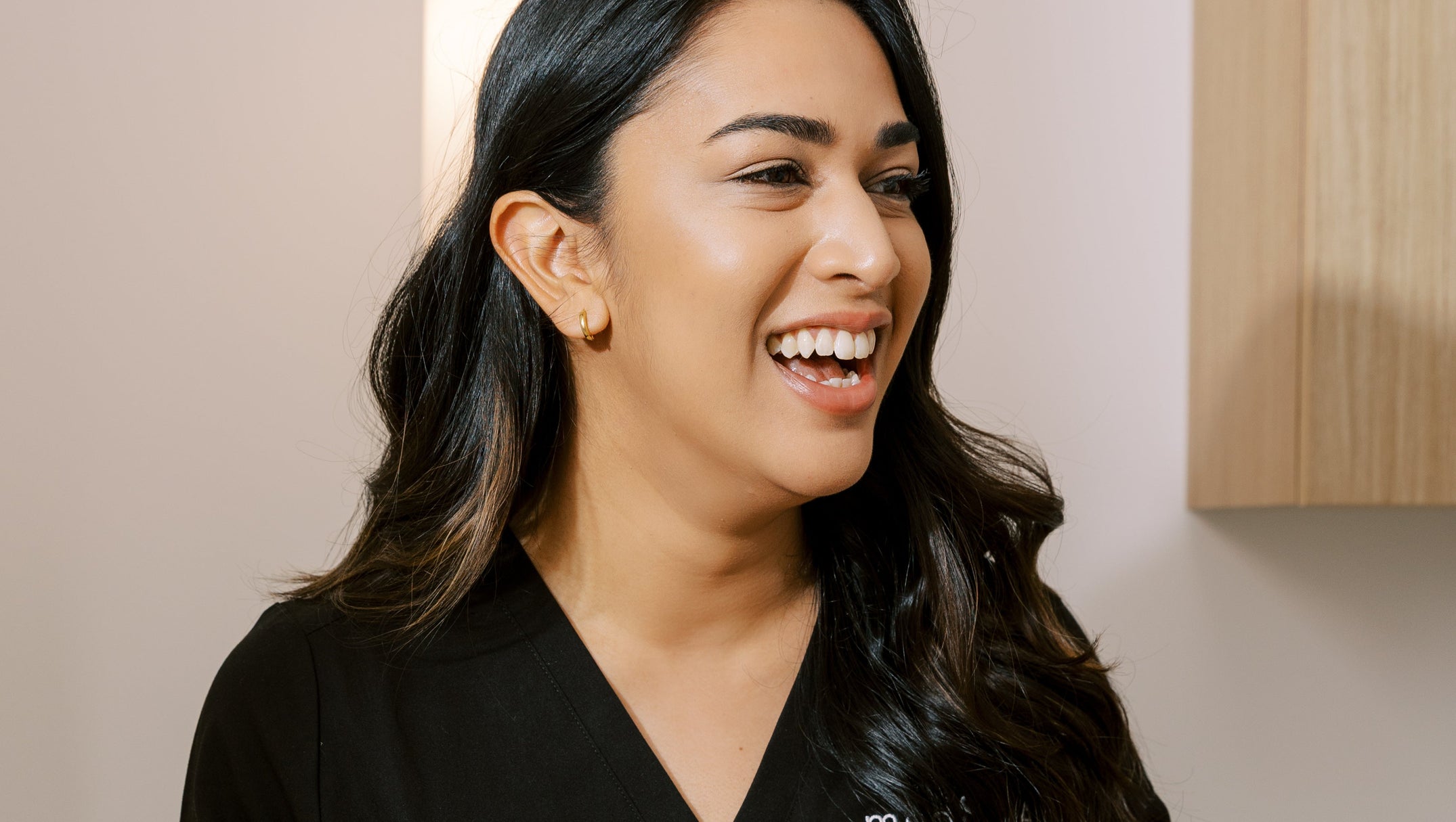 med spa provider wearing a black scrubs with the milk and honey logo, standing in a med spa treatment room.