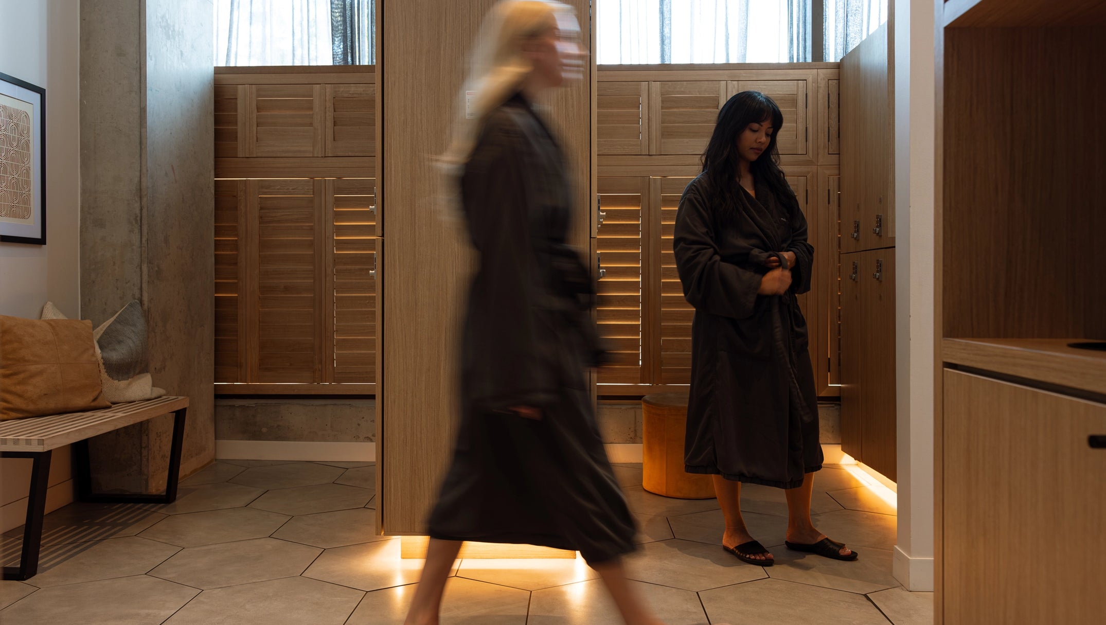 Two women in a room with wooden lockers and a bench.