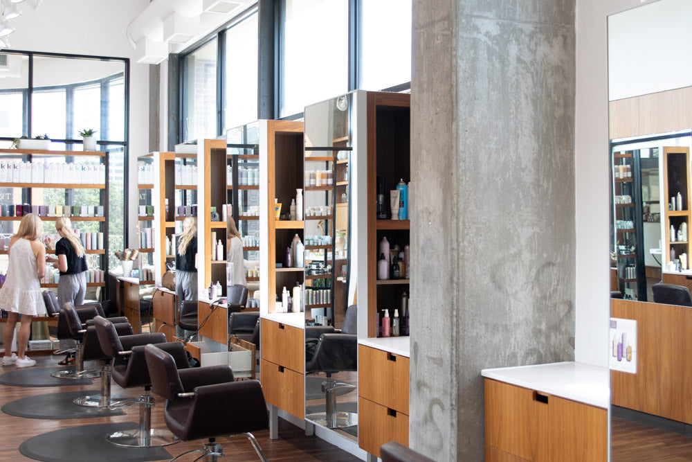 Modern hair salon interior with chairs, mirrors, and shelves.