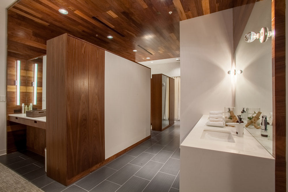 A modern bathroom interior with dark wood cabinetry, a white vanity, gray floor tiles, and a large wall mirror.