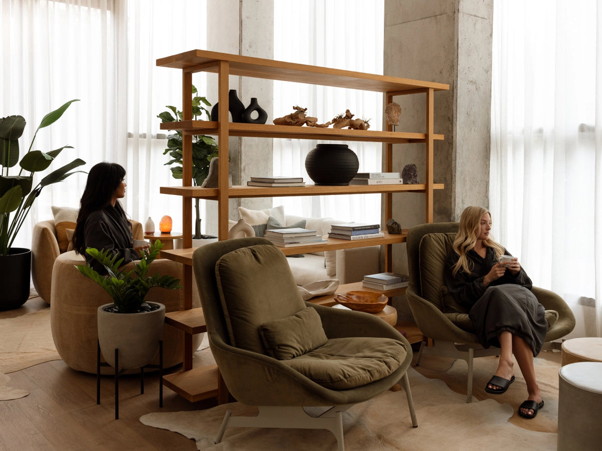 Two women in a modern living room with a wooden bookshelf and comfortable chairs.
