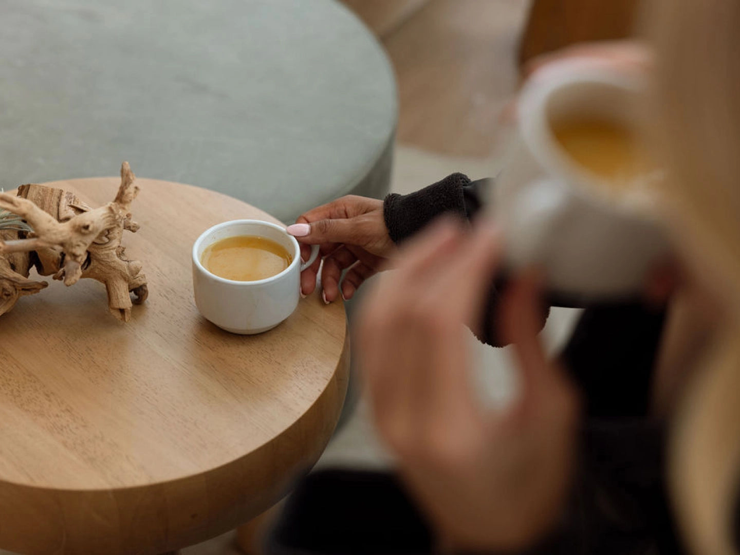 Two people sitting at a table with coffee cups, one of which is being held.