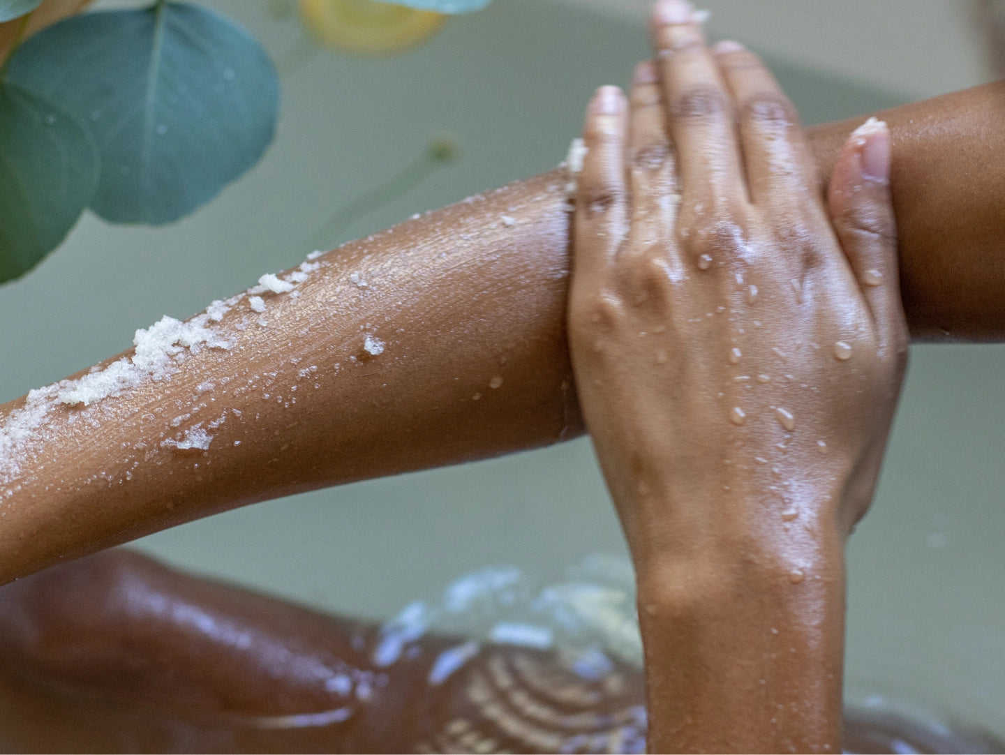 Person scrubbing their arm with a scrubber, with water droplets visible.