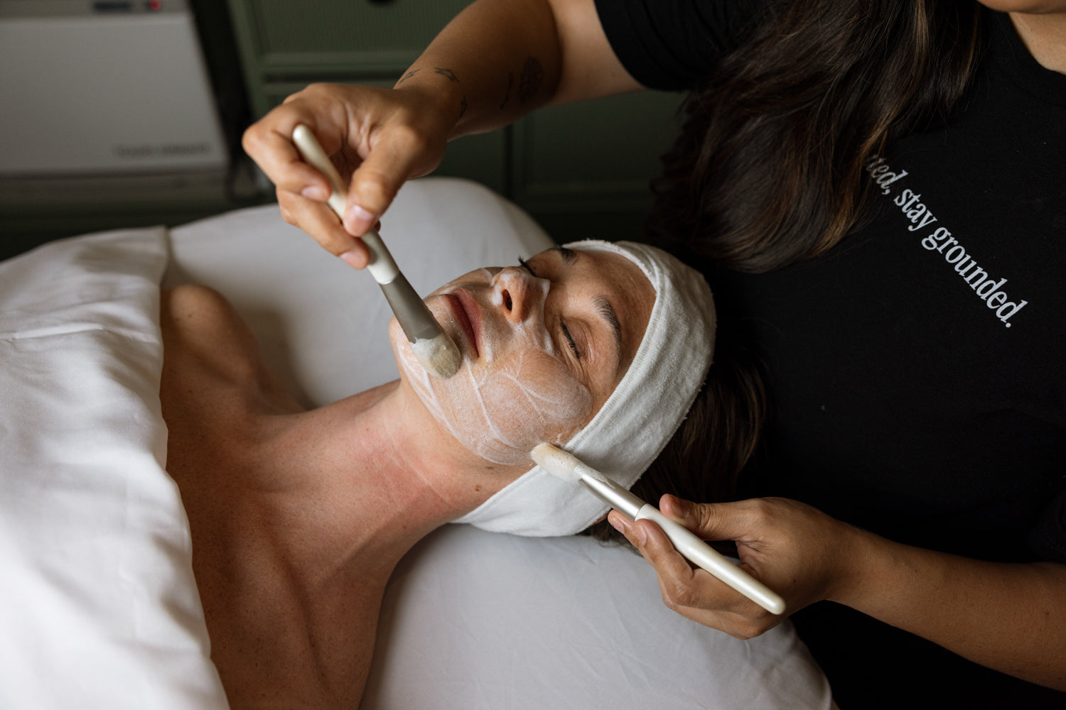 Person receiving a facial treatment with a towel on their head and a brush applying product.