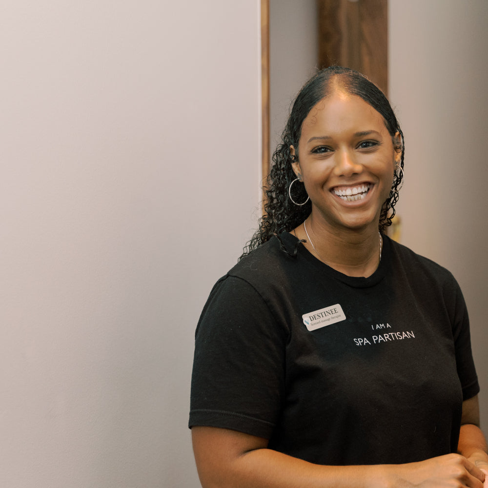 Woman wearing a black shirt with text, standing indoors against a neutral background