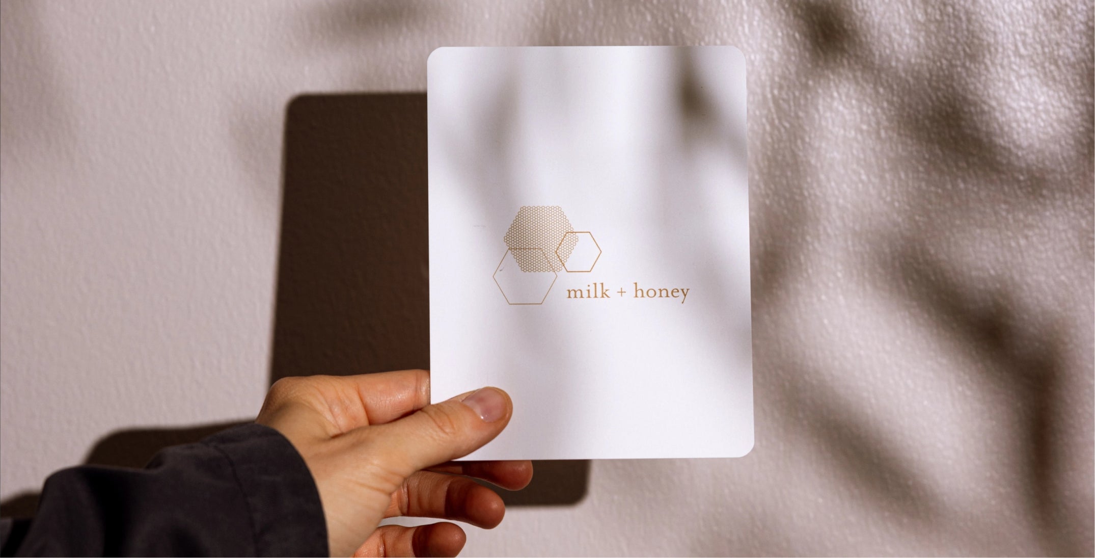 Hand holding a 'milk + honey' sheet mask against a neutral background